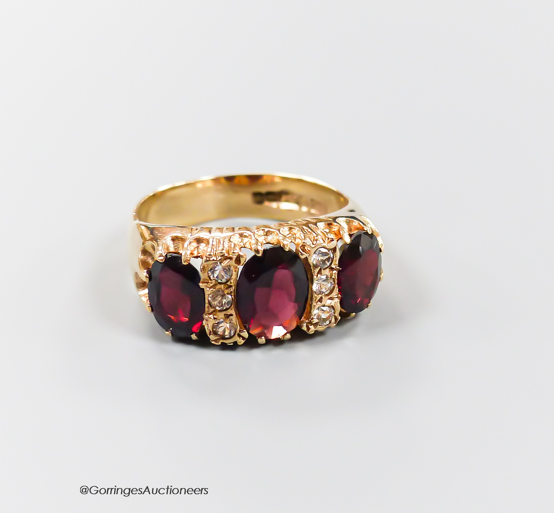 A modern 9ct gold and graduated three stone garnet set half hoop dress ring, with diamond chip spacers, size N, gross 4.9 grams.
